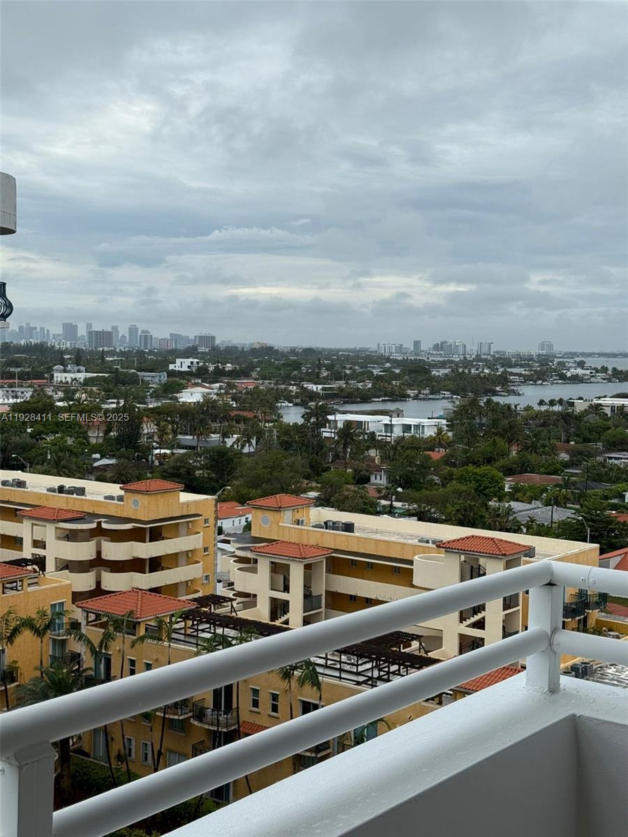 A high-angle view from a balcony overlooks a residential area, waterway, and distant city skyline — 8911 Collins Ave # 1103, Surfside FL 33154, SURFSIDE, FL