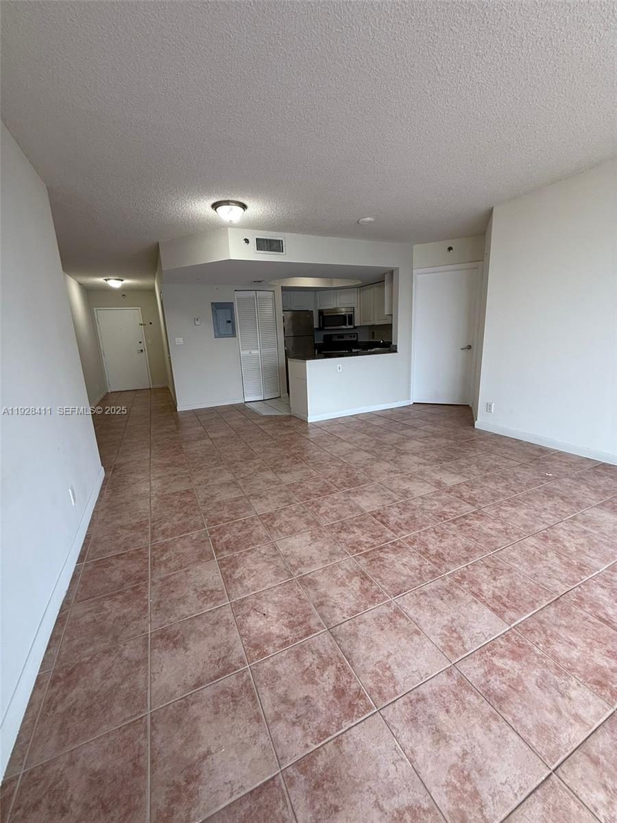 An open-concept living area features tan tile flooring, white walls, and a pass-through kitchen — 8911 Collins Ave # 1103, Surfside FL 33154, SURFSIDE, FL