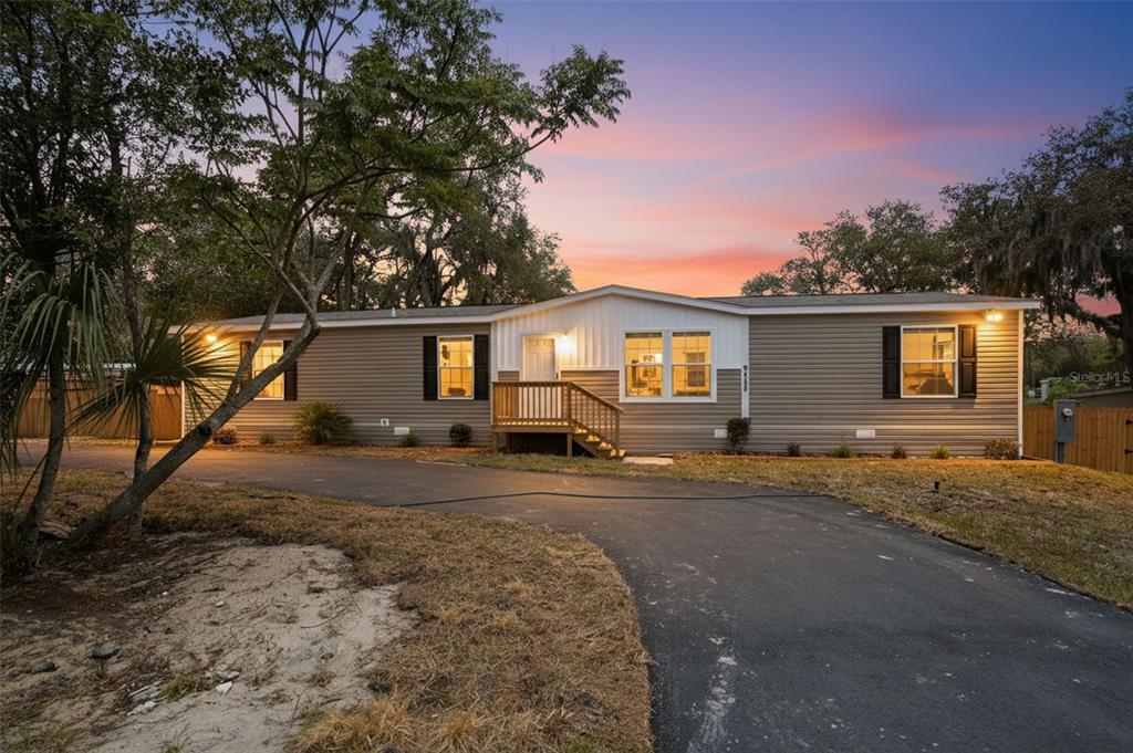 A single-story manufactured home with tan siding, black shutters, and a wooden front porch — 9533 ROUND LAKE DRIVE, WEEKI WACHEE, FL