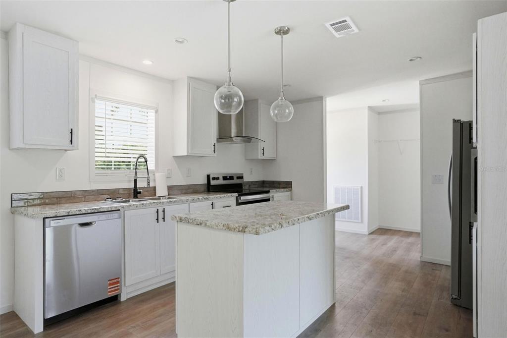 A modern kitchen features white cabinets, granite countertops, a center island, and stainless steel appliances — 9533 ROUND LAKE DRIVE, WEEKI WACHEE, FL