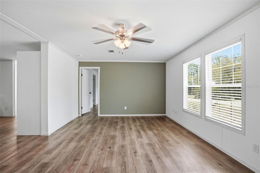 An empty room features light wood-look flooring, white walls, and a green accent wall — 9533 ROUND LAKE DRIVE, WEEKI WACHEE, FL