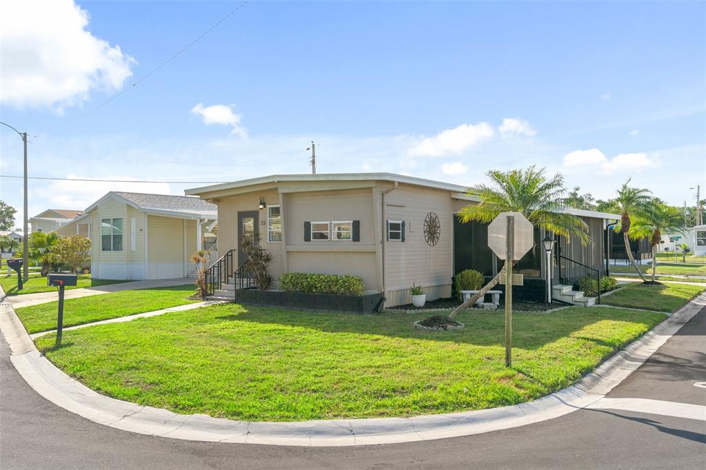 A tan manufactured home with a screened porch sits on a corner lot with grass — 2900 8TH AVENUE W UNIT 23, PALMETTO, FL