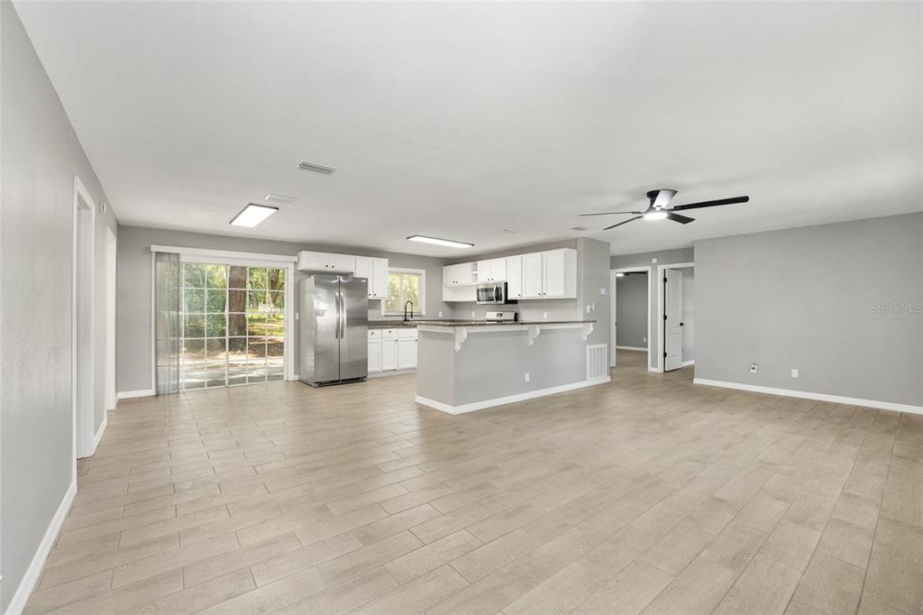An open-concept kitchen and living area with white cabinets, stainless steel appliances, and tile flooring — 5805 NW 16TH STREET, OCALA, FL