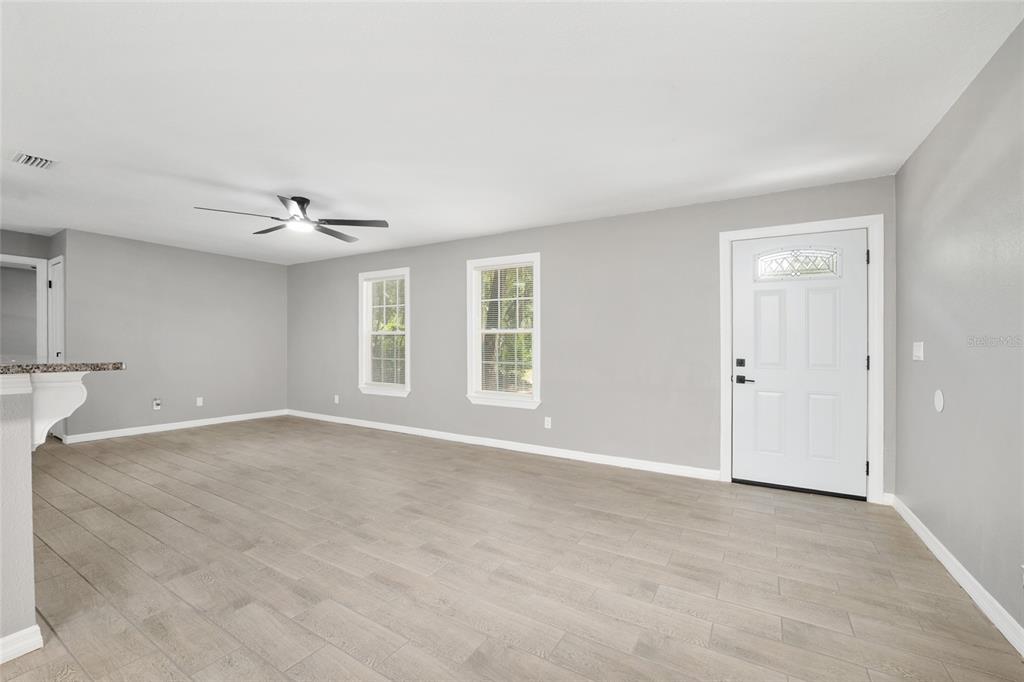 An empty living room with gray walls, light wood-look tile flooring, and a white door — 5805 NW 16TH STREET, OCALA, FL