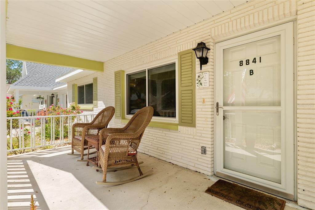 A covered front porch features two wicker rocking chairs, white brick walls, and a door — 8841 SW 91ST STREET UNIT B, OCALA, FL