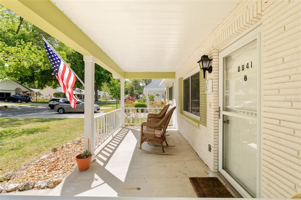 A covered front porch features white railings, two wicker rocking chairs, and an American flag — 8841 SW 91ST STREET UNIT B, OCALA, FL