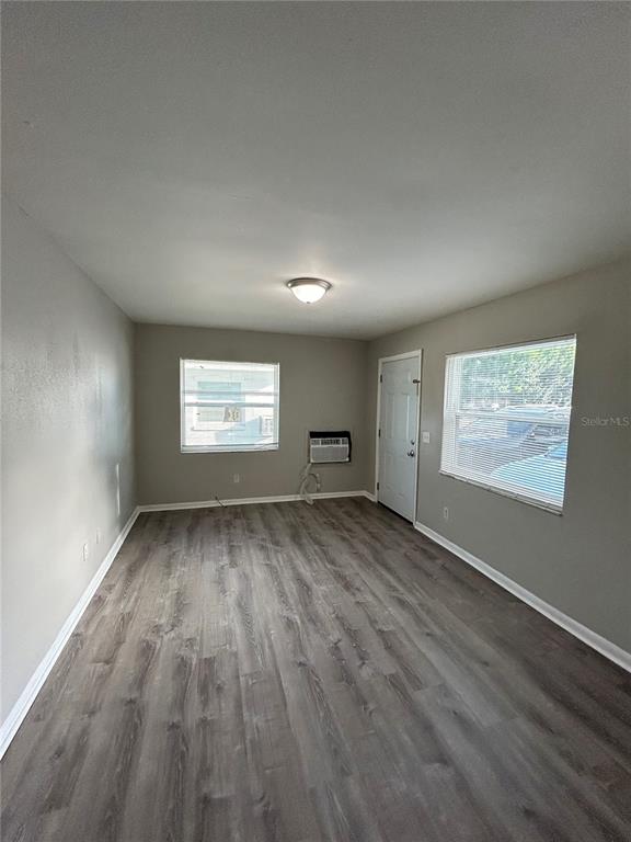 An empty room features gray wood-look flooring, light gray walls, two windows, and a door — 1484 32ND STREET NW, WINTER HAVEN, FL