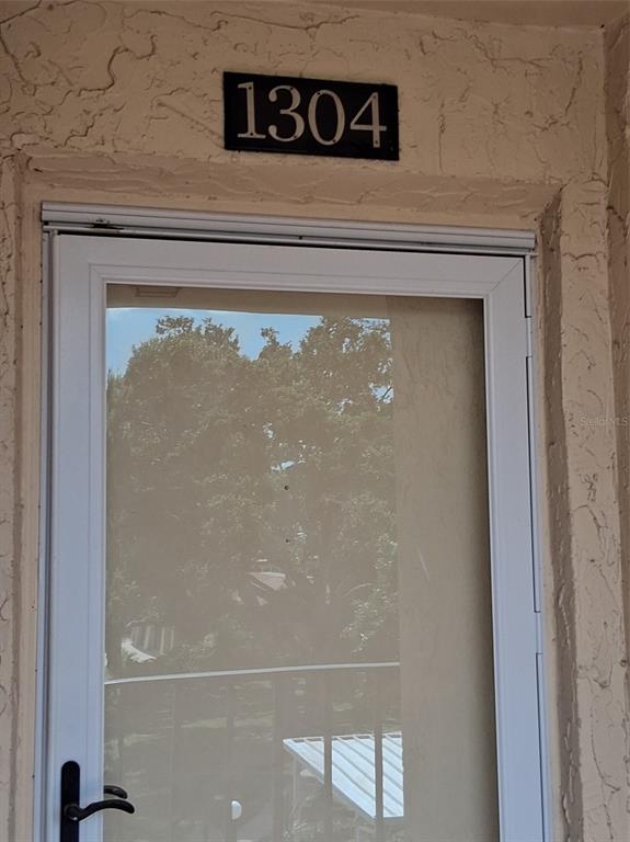 A white storm door is mounted on a textured beige wall below a house number — 12200 VONN ROAD UNIT 1304, LARGO, FL