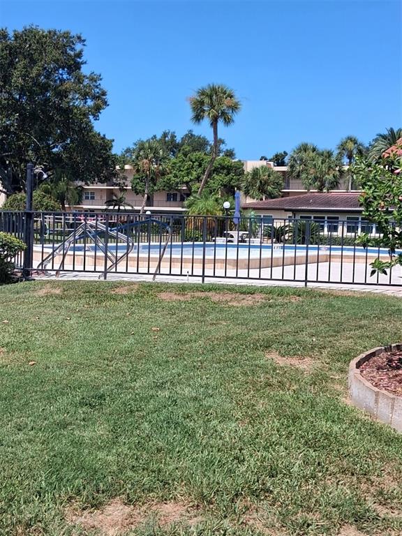 A fenced outdoor swimming pool is surrounded by green grass and palm trees — 12200 VONN ROAD UNIT 1304, LARGO, FL