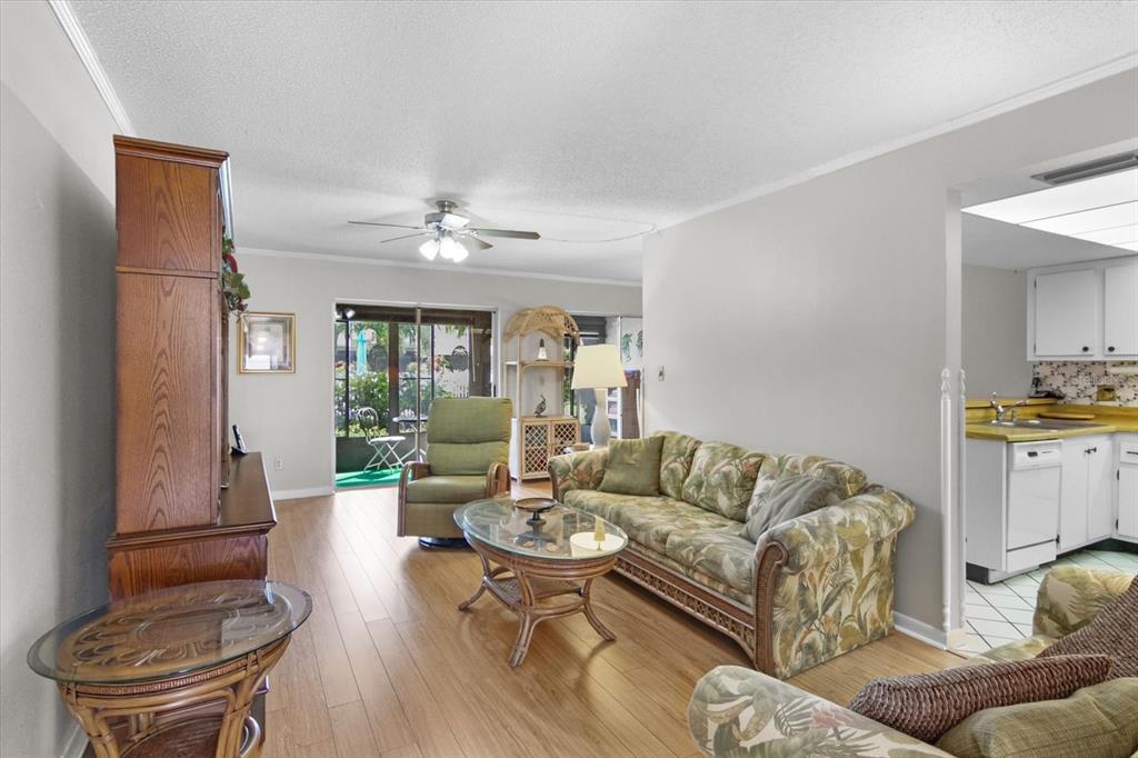 A living room with wood-look flooring, a floral sofa, and an adjacent kitchen — 6108 7TH AVENUE W UNIT 6108, BRADENTON, FL