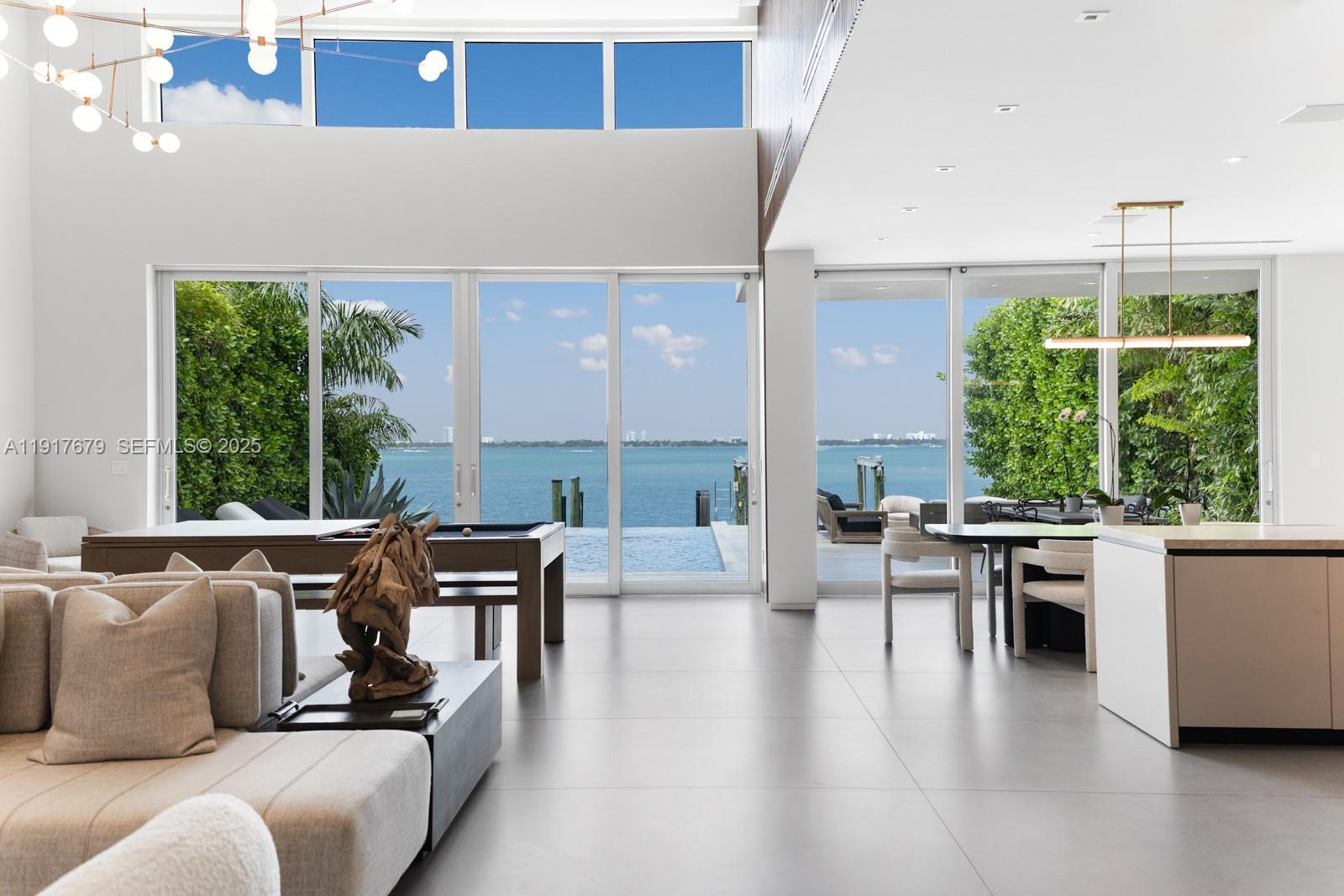 A modern open-concept living area features a pool table, dining space, and expansive water views — 1379 N Venetian Way, Miami FL 33139, MIAMI, FL