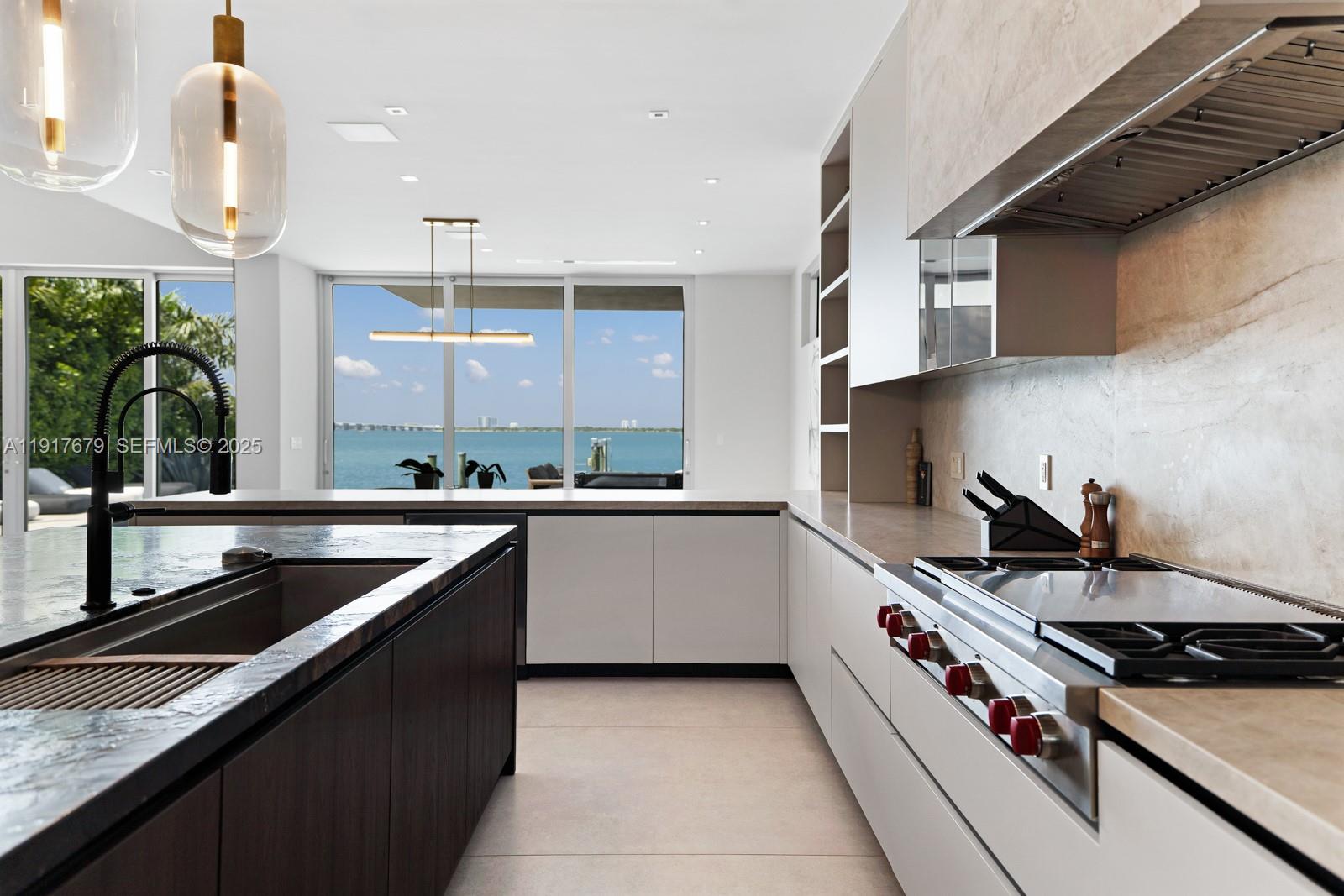 A modern kitchen features a dark wood island, light cabinetry, and a view of the ocean — 1379 N Venetian Way, Miami FL 33139, MIAMI, FL