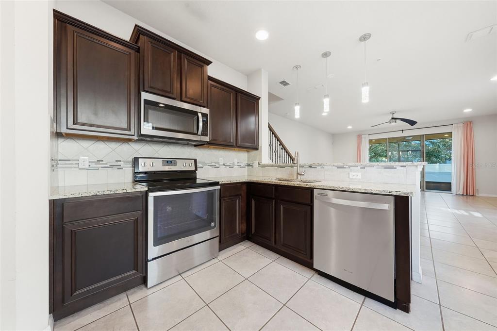A kitchen with dark wood cabinets, stainless steel appliances, and granite countertops — 1096 PAVIA DRIVE, APOPKA, FL