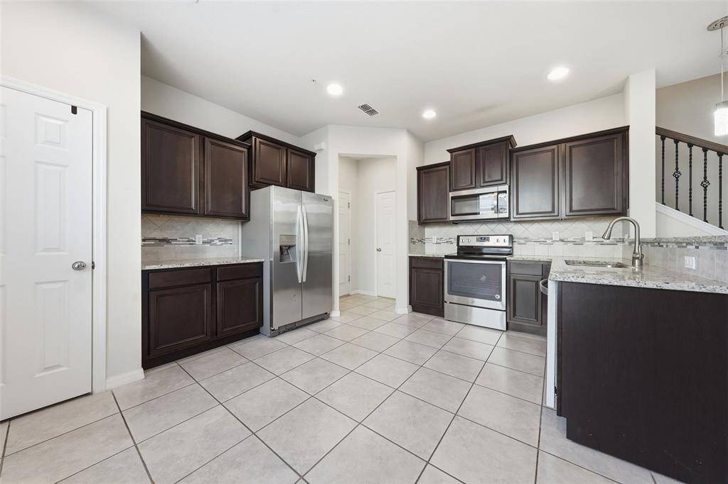 A kitchen with dark wood cabinets, stainless steel appliances, granite countertops, and light tile flooring — 1096 PAVIA DRIVE, APOPKA, FL