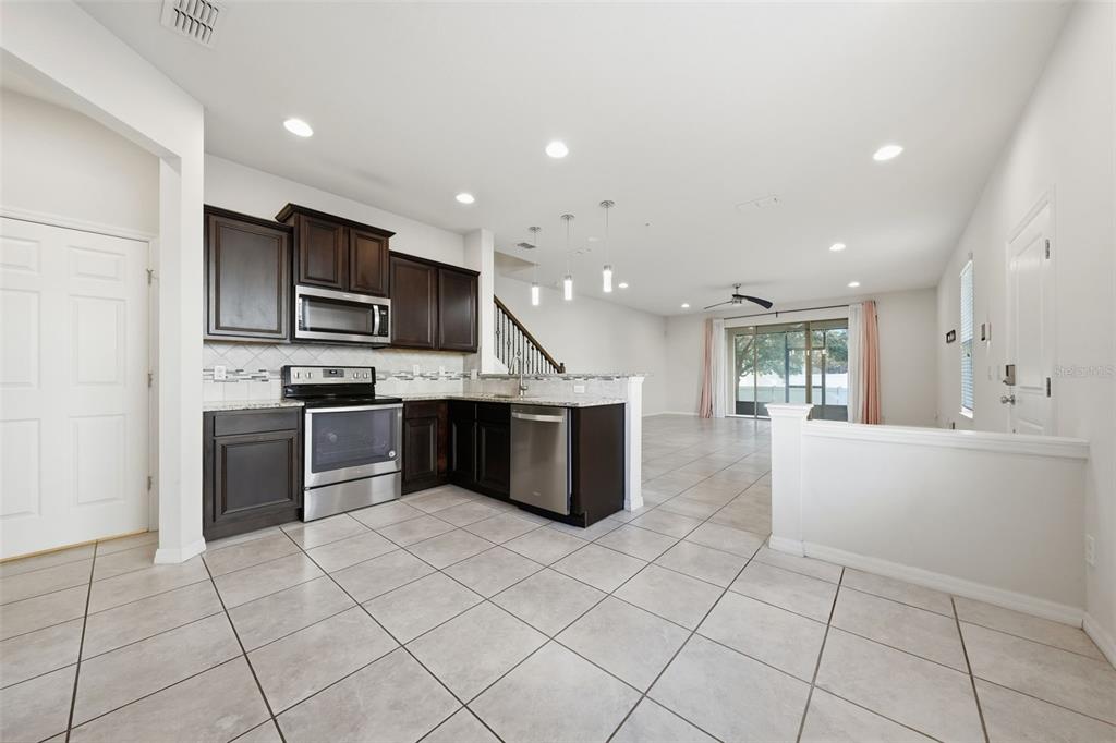 A kitchen with dark wood cabinets, stainless steel appliances, and tile flooring opens to a living area — 1096 PAVIA DRIVE, APOPKA, FL