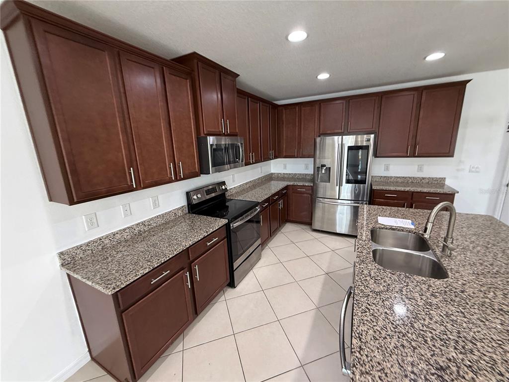 A kitchen features dark wood cabinets, granite countertops, stainless steel appliances, and tiled flooring — 11301 HUDSON HILLS LANE, RIVERVIEW, FL