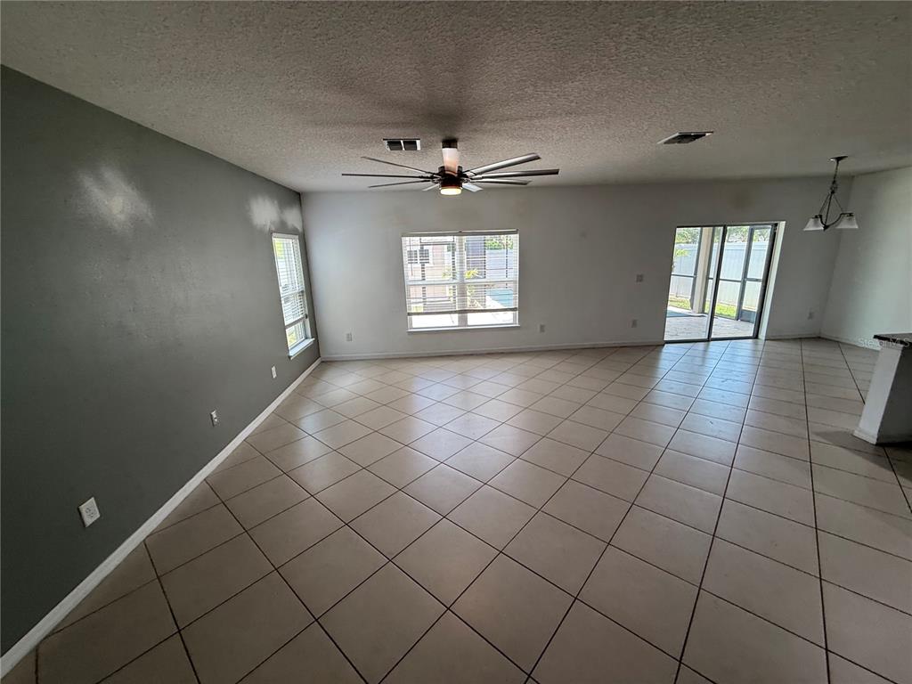 An open-concept living area features light-colored tile flooring, a ceiling fan, and a gray accent wall — 11301 HUDSON HILLS LANE, RIVERVIEW, FL
