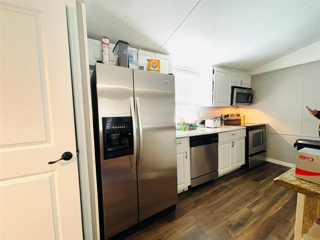 A kitchen features stainless steel appliances, white cabinets, and wood-look flooring — 4503 USHER AVENUE, ORLANDO, FL