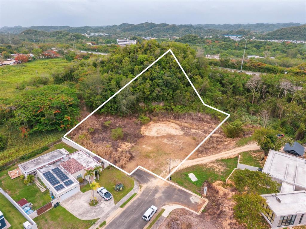 An aerial view shows a vacant, irregularly shaped residential lot bordered by trees and houses — URB. REPARTO ROSELLO, MANATI, PR