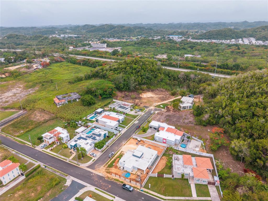 An aerial view shows a residential neighborhood with several houses, paved streets, and surrounding hills — URB. REPARTO ROSELLO, MANATI, PR