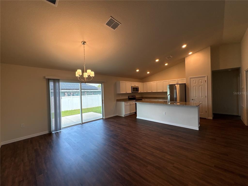 An open-concept kitchen and living area feature wood-look flooring, white cabinetry, and sliding glass doors — 3491 SW 155TH LANE, OCALA, FL