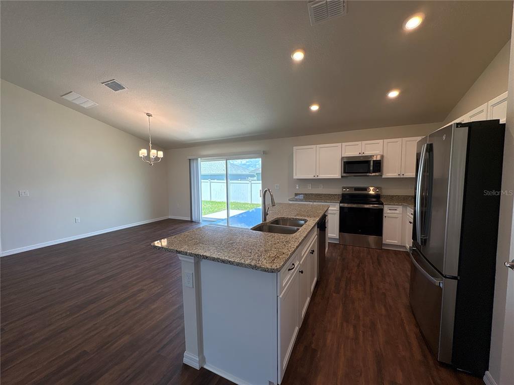 A kitchen with white cabinets, granite countertops, and stainless steel appliances opens to a living area — 3491 SW 155TH LANE, OCALA, FL