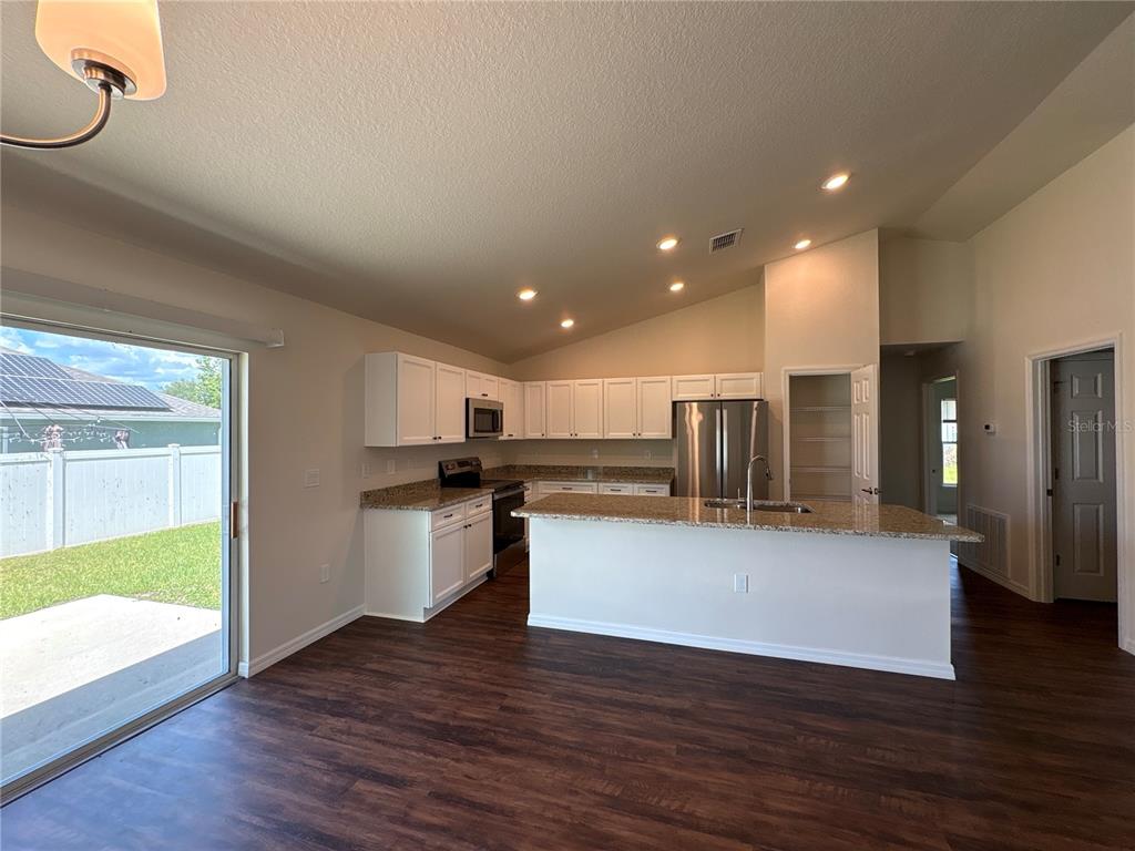 A kitchen with white cabinets, granite countertops, stainless steel appliances, and dark wood-look flooring — 3491 SW 155TH LANE, OCALA, FL