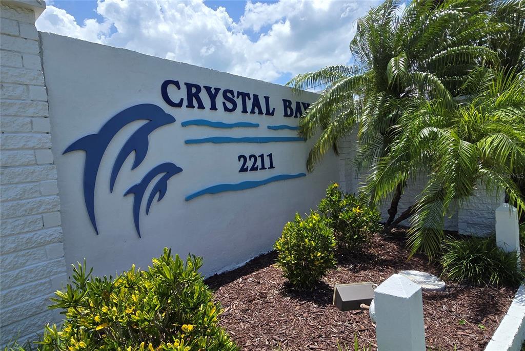 A white wall features the blue text Crystal Bay, a dolphin logo, and the number 2211 — 9 YAWL LANE UNIT 9, PALM HARBOR, FL