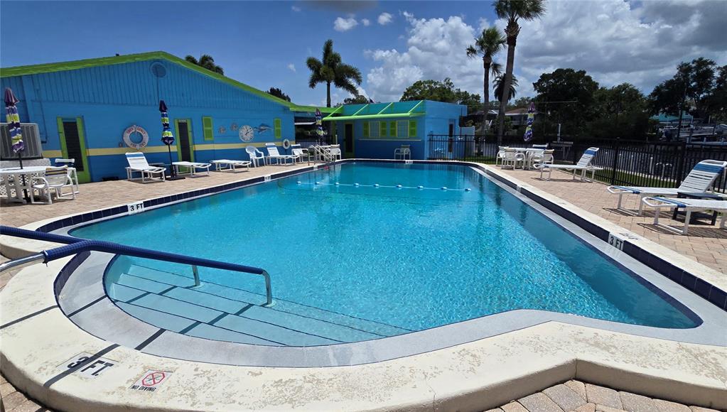 An outdoor swimming pool is surrounded by a paved deck, lounge chairs, and blue buildings — 9 YAWL LANE UNIT 9, PALM HARBOR, FL