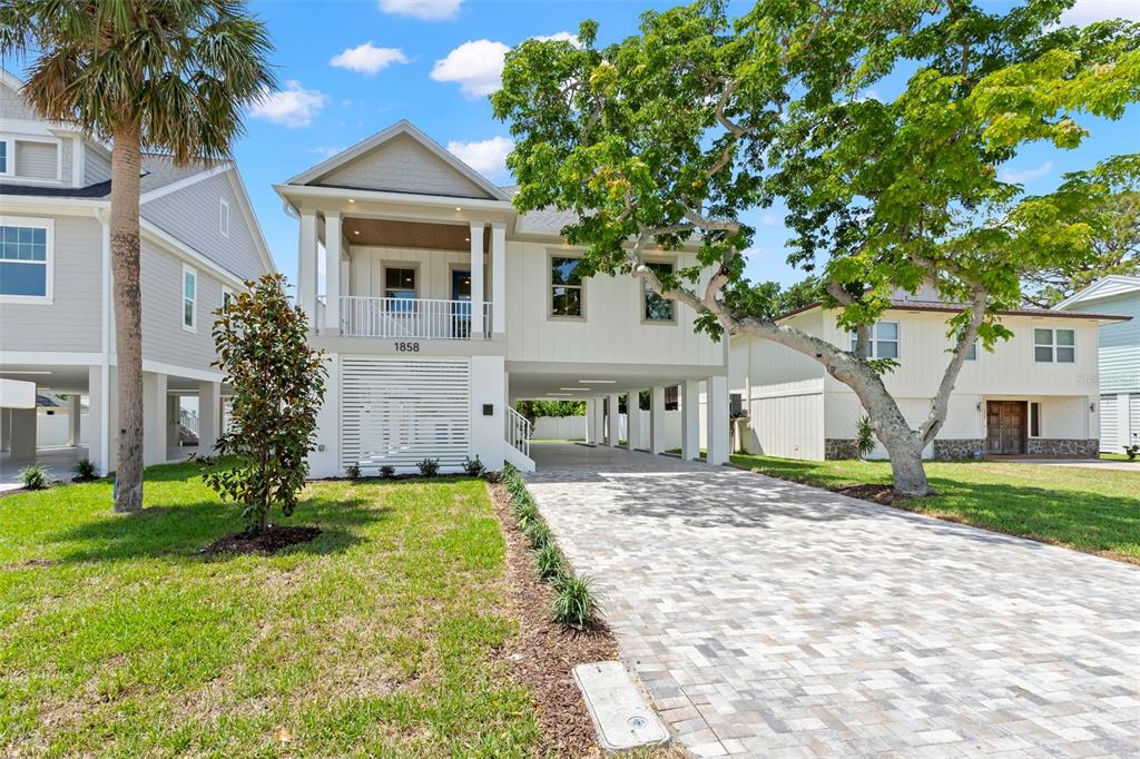 A two-story elevated house with a paved driveway and a front porch under a blue sky — 1858 MISSISSIPPI AVENUE NE, ST PETERSBURG, FL