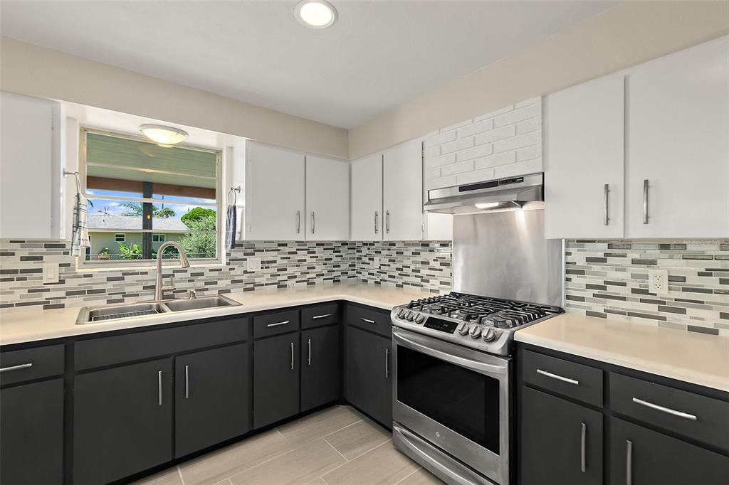 A kitchen features white upper cabinets, dark lower cabinets, a gas range, and a tiled backsplash — 1662 LOUISIANA ROAD, SOUTH DAYTONA, FL
