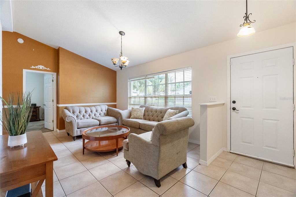 A living room features beige tile floors, a tan accent wall, and neutral upholstered furniture — 1219 MAYBROOK STREET S, APOPKA, FL