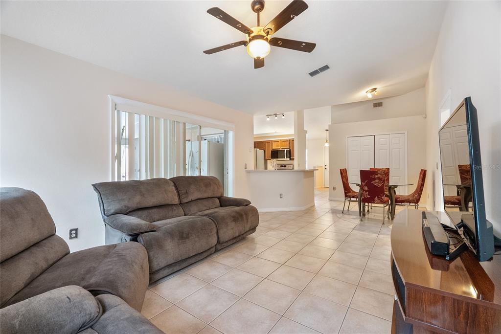 A living room with tile floors, a ceiling fan, and an open kitchen in the background — 1219 MAYBROOK STREET S, APOPKA, FL