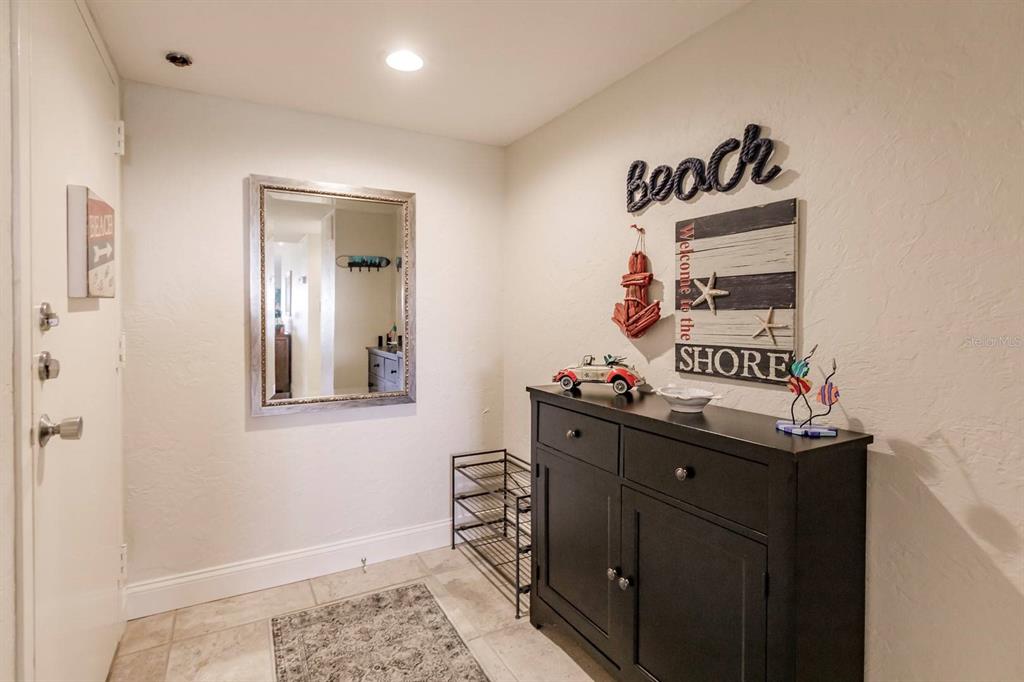 An entryway features a black cabinet, a wall mirror, and beach-themed wall decor — 1125 W PEPPERTREE DRIVE UNIT 605, SARASOTA, FL
