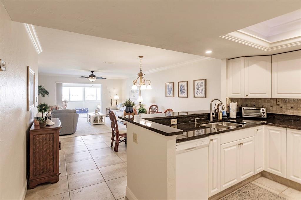 A kitchen with white cabinets and dark countertops overlooks an open-concept living and dining area — 1125 W PEPPERTREE DRIVE UNIT 605, SARASOTA, FL