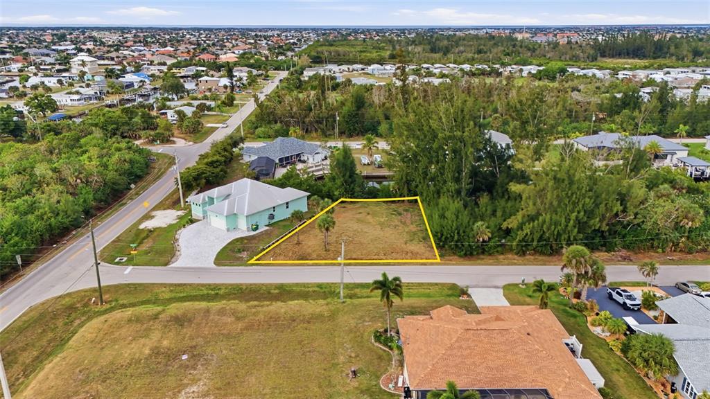 An aerial view shows a vacant, yellow-outlined residential lot situated between two houses — 3925 MAGNOLIA WAY, PUNTA GORDA, FL