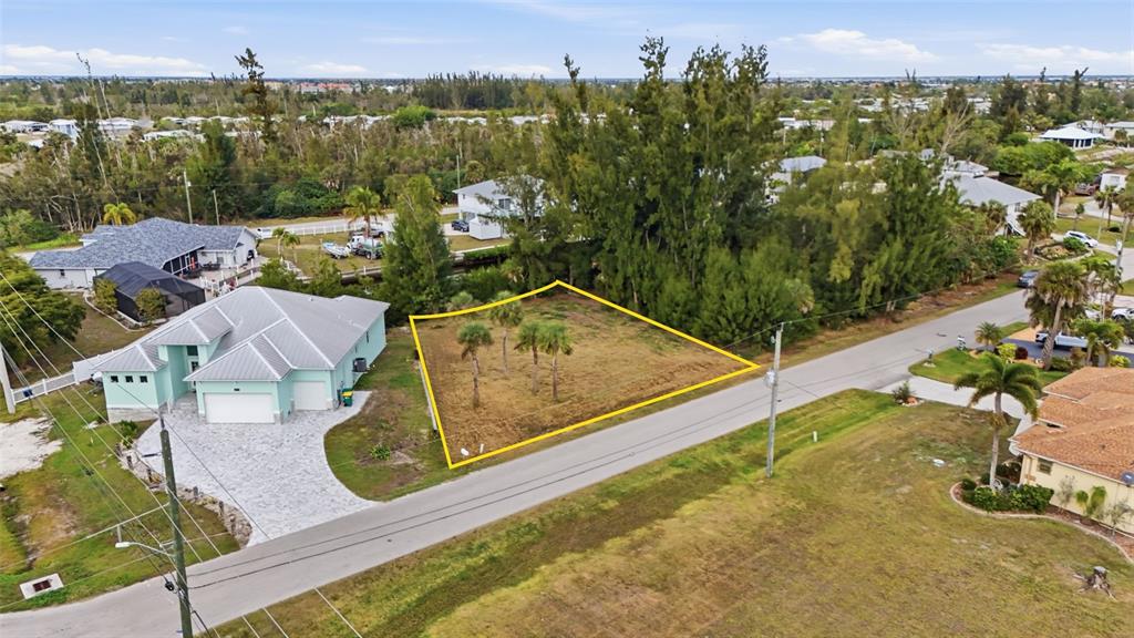 An aerial view shows a vacant, yellow-outlined residential lot situated between two houses — 3925 MAGNOLIA WAY, PUNTA GORDA, FL