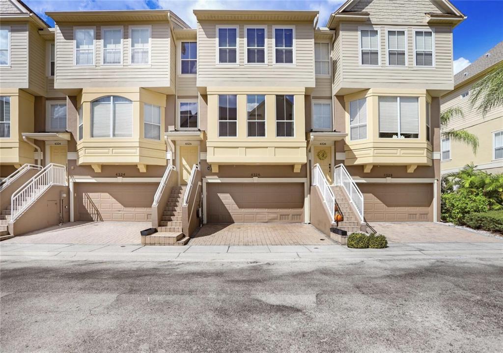Three attached townhouses feature beige siding, bay windows, and ground-level garages with front staircases — 4326 SPINNAKER COVE LANE, TAMPA, FL