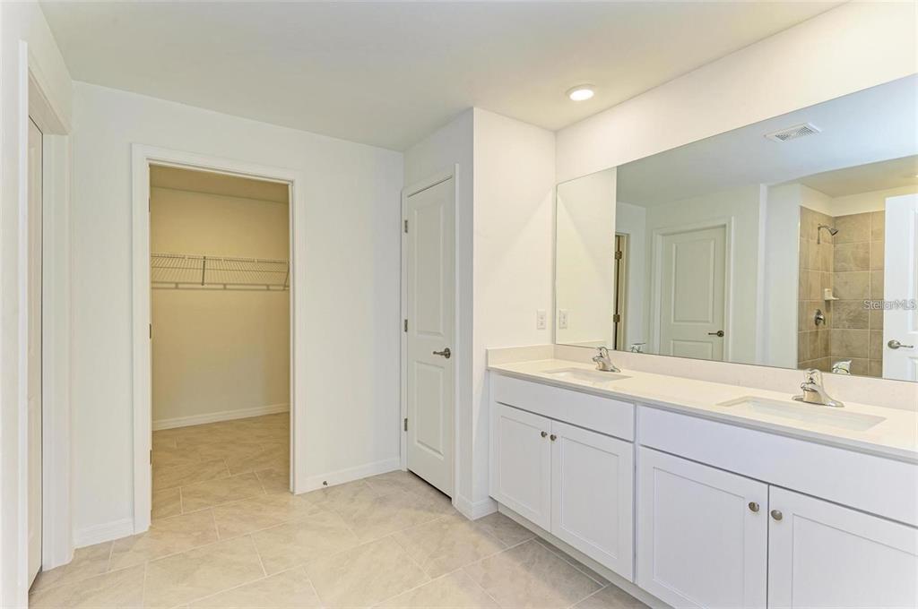 A bathroom features a double vanity with white cabinets, a large mirror, and a walk-in closet — 1485 PULASKI STREET, PORT CHARLOTTE, FL