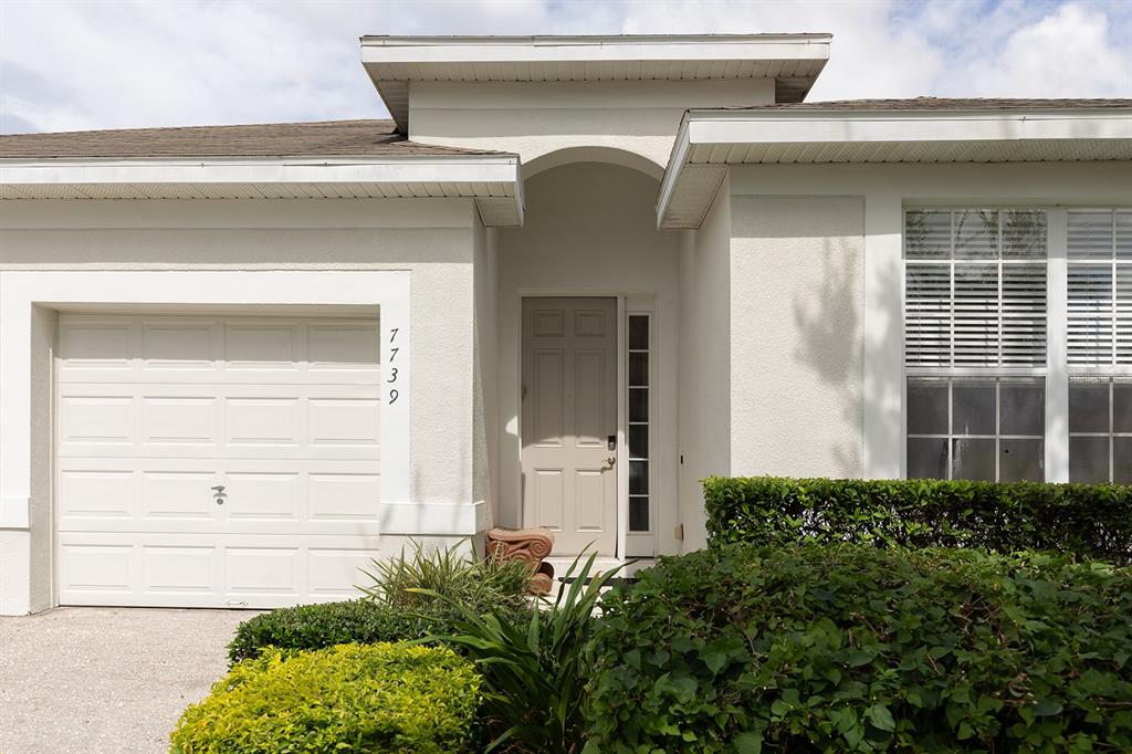 The exterior of a single-story house features a white stucco facade, a garage, and landscaping — 7739 TEASCONE BOULEVARD, KISSIMMEE, FL