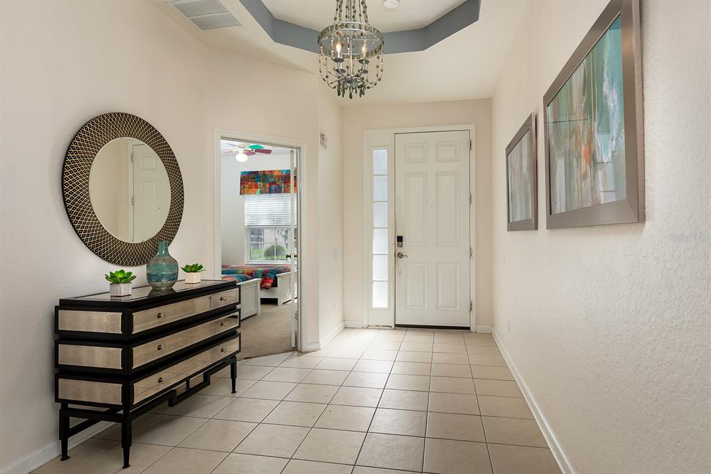 A tiled entryway features a mirrored chest, a round wall mirror, and a crystal chandelier — 7739 TEASCONE BOULEVARD, KISSIMMEE, FL
