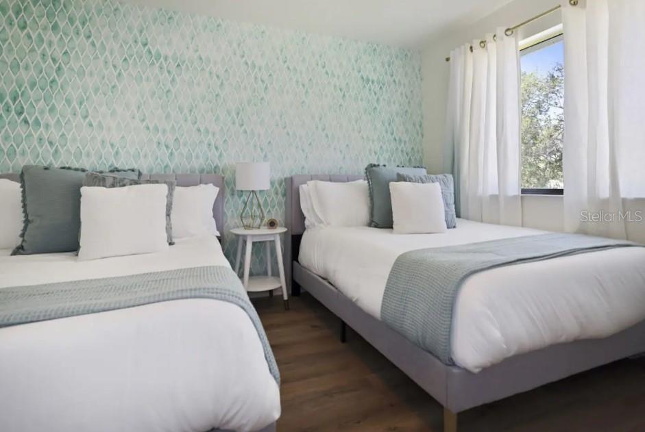 A bedroom features two beds with gray frames, white bedding, and a teal patterned accent wall — 10075 W BAY STREET, SEMINOLE, FL