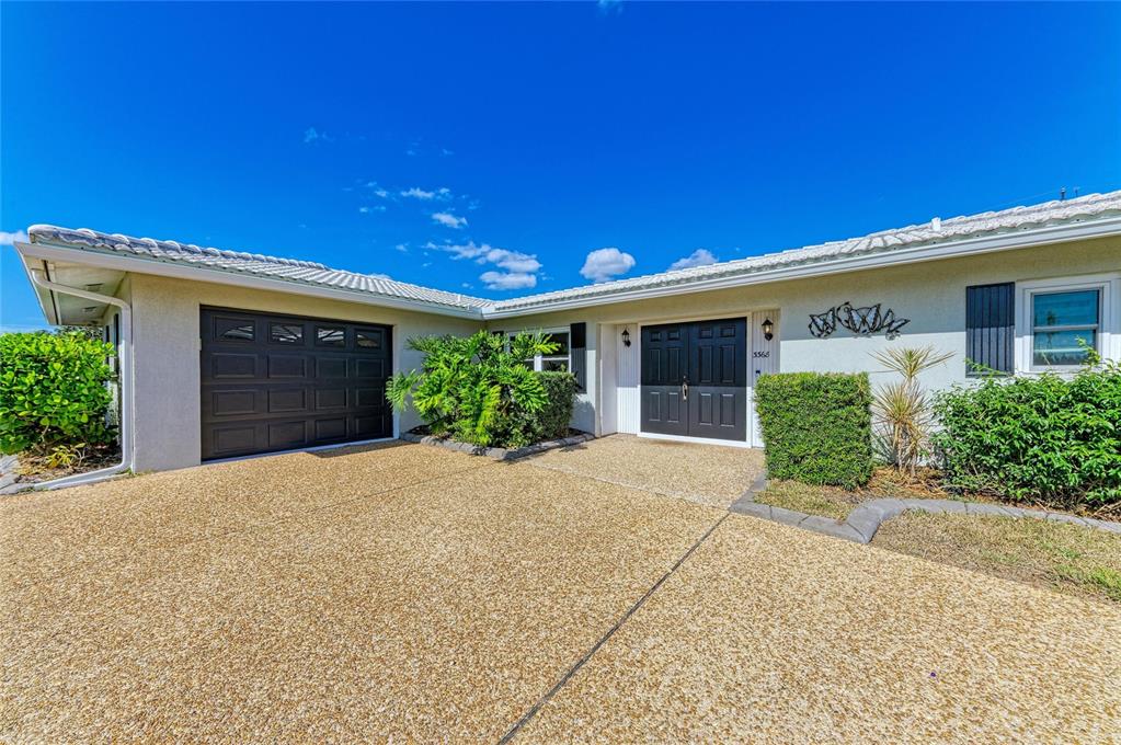 A single-story house exterior features a dark garage door, double front doors, and gravel driveway — 3368 SHEFFIELD CIRCLE, SARASOTA, FL