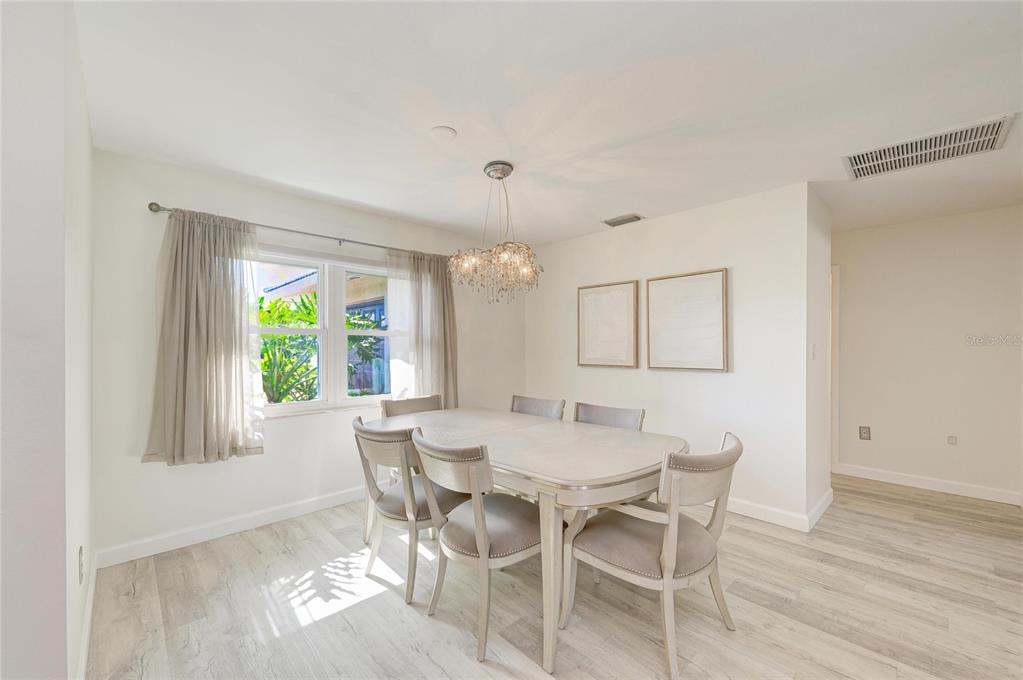A dining room features a light wood table, upholstered chairs, a crystal chandelier, and windows — 3368 SHEFFIELD CIRCLE, SARASOTA, FL