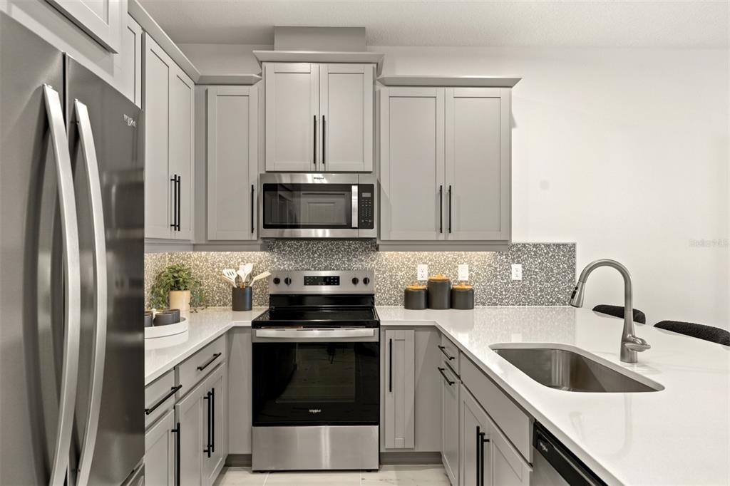 A modern kitchen features gray cabinets, stainless steel appliances, white countertops, and a tiled backsplash — 5168 GREENSHADE GROVE AVENUE, APOPKA, FL