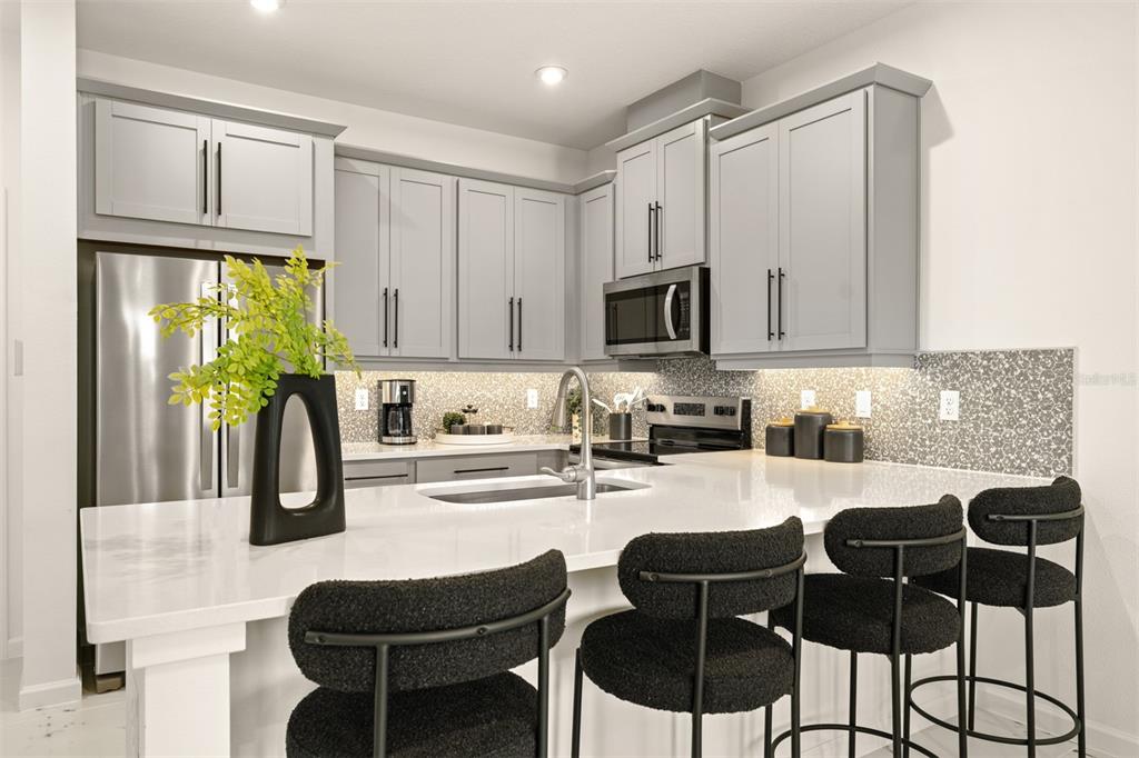 A modern kitchen features gray cabinets, white countertops, a tiled backsplash, and four black stools — 5168 GREENSHADE GROVE AVENUE, APOPKA, FL