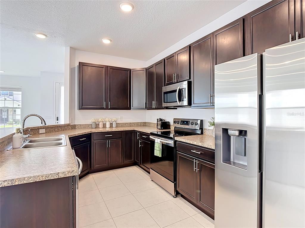 A kitchen features dark wood cabinets, stainless steel appliances, and beige laminate countertops — 148 BOYDFIELD LANE, DAVENPORT, FL