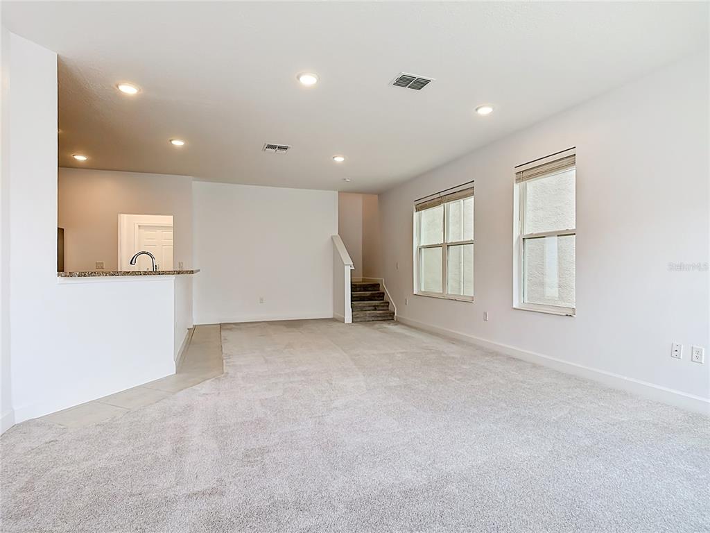 A carpeted living room features a kitchen counter, stairs, and two windows — 148 BOYDFIELD LANE, DAVENPORT, FL