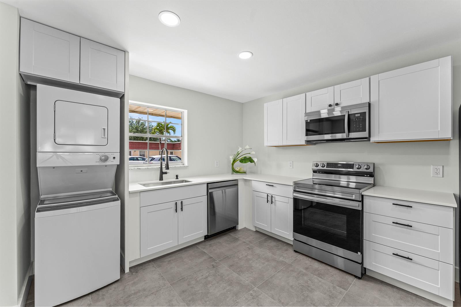 A kitchen features white cabinets, stainless steel appliances, a stacked washer-dryer, and gray tile flooring — 711 Laconia Circle # B, FL 33467, FL