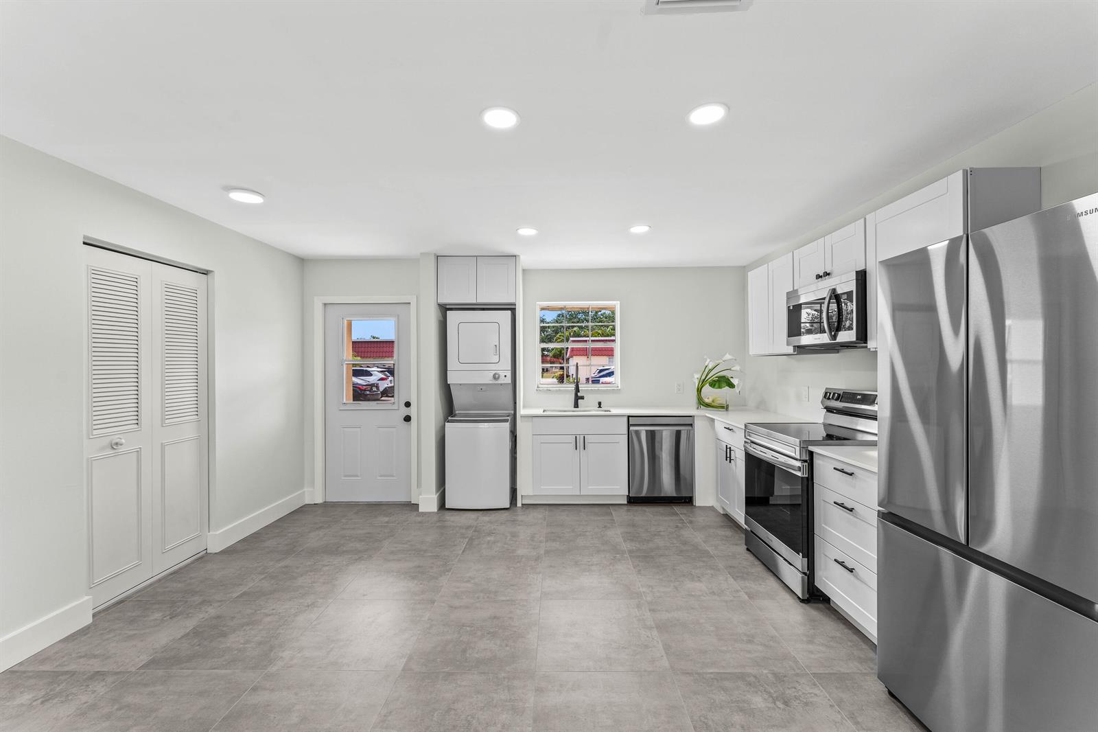 A modern kitchen features white cabinetry, stainless steel appliances, gray tile flooring, and laundry units — 711 Laconia Circle # B, FL 33467, FL